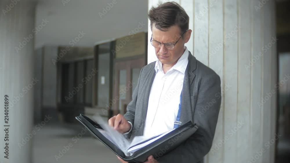 a young, respectable businessman sent to an office building. In his hands he holds a briefcase, looks through documents. a young, respectable businessman sent to an office building. In his hands he holds a briefcase, looks through documents.