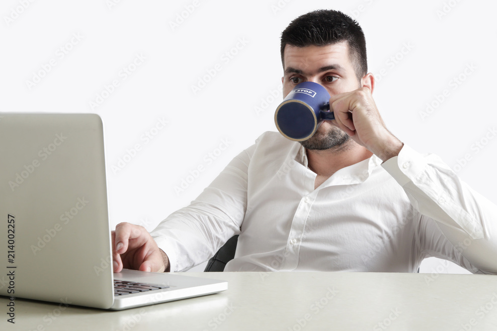 Young businessman drinking his coffee in front of laptop, studio shot, office life Young businessman drinking his coffee in front of laptop, studio shot, office life