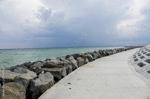 Background of the sea wave in summer. Water landscape with clouds on the horizon. Sea nature of tranquility. An alarming sky. Stones by the water  a concrete path along the sea.