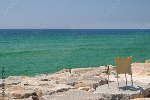 Paisagem maritima com cadeira para sentar deixada em cima de rochas