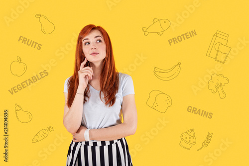 Clever nutritionist. Pretty young nutritionist smiling and thoughtfully touching her face while waiting for a client