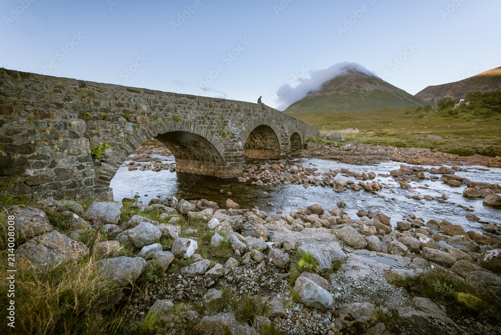 A person sits on the edge of the edge of the Sligachan Old Bridge on the Isle of Skye, Scotland