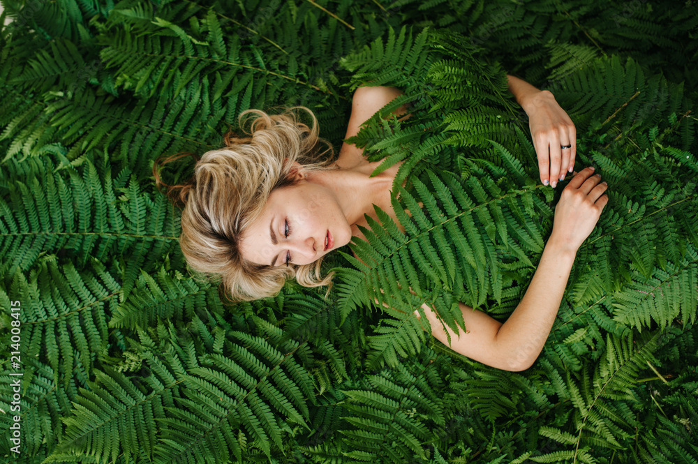 A beautiful girl lies in a fern.