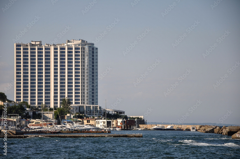 Embankment of the Black Sea. Small waves and a beautiful panorama of the sea. Classical and modern buildings. The slopes are covered with green trees. Light wind and good weather. Embankment of the Black Sea. Small waves and a beautiful panorama of the sea. Classical and modern buildings. The slopes are covered with green trees. Light wind and good weather.