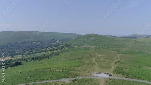 wide aerial shot of Bonehill Rocks in the background and the road, carpark, and a car driving from left to right in the foreground. Dartmoor, England photo