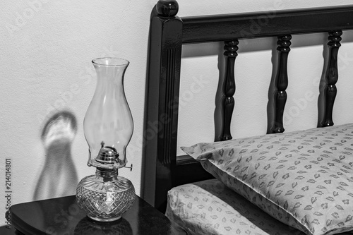 Vintage flat-wick Kerosene Oil Lamp on bedside table, bed headboard, pillow, mattress, bedroom.