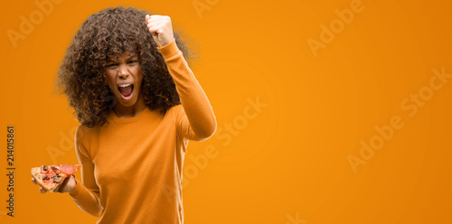 African american woman with a pizza slice annoyed and frustrated shouting with anger, crazy and yelling with raised hand, anger concept