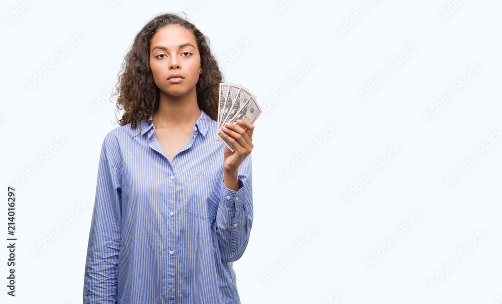 Obraz premium Young hispanic woman holding dollars with a confident expression on smart face thinking serious