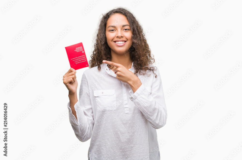Young hispanic woman holding passport of Switzerland very happy pointing with hand and finger Young hispanic woman holding passport of Switzerland very happy pointing with hand and finger