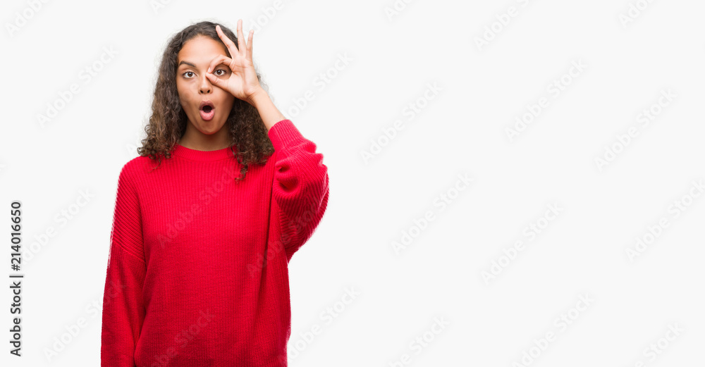 Young hispanic woman wearing red sweater doing ok gesture shocked with surprised face, eye looking through fingers. Unbelieving expression. Young hispanic woman wearing red sweater doing ok gesture shocked with surprised face, eye looking through fingers. Unbelieving expression.