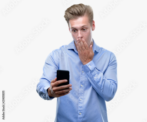 Young handsome blond man using smartphone cover mouth with hand shocked with shame for mistake, expression of fear, scared in silence, secret concept