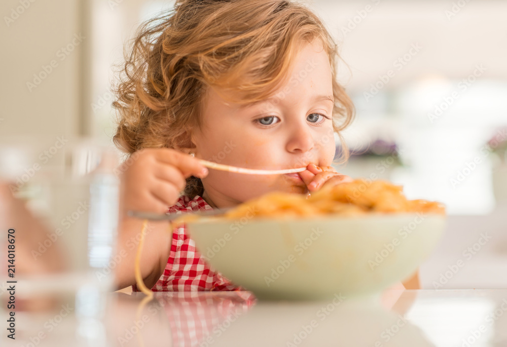 Beautiful blond child eating spaghetti with hands at home