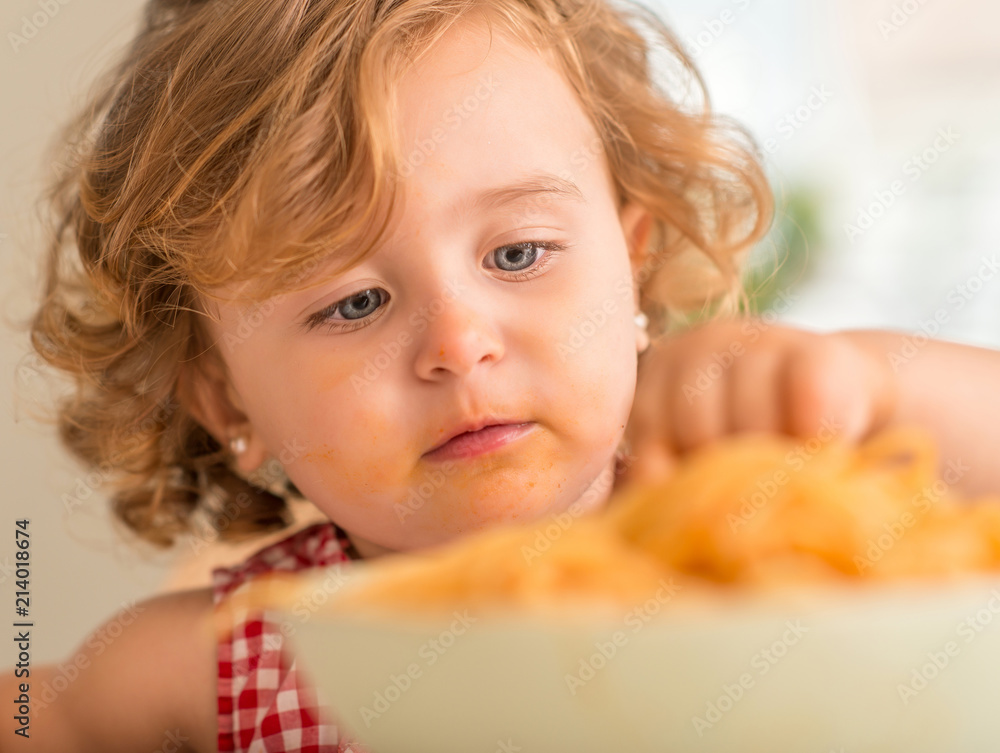 Beautiful blond child eating spaghetti with hands at home Beautiful blond child eating spaghetti with hands at home