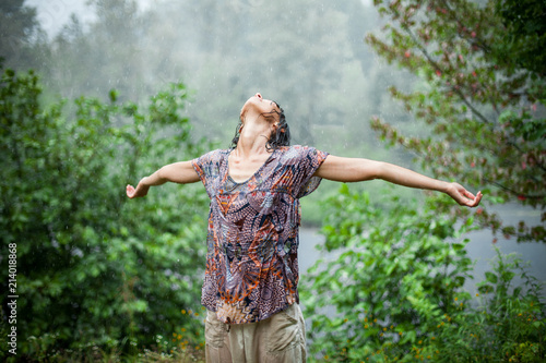Woman with opened arms and head tilted back standing and enjoying the rain