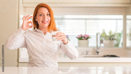 Thirsty redhead woman and glass of water doing ok sign with fingers, excellent symbol