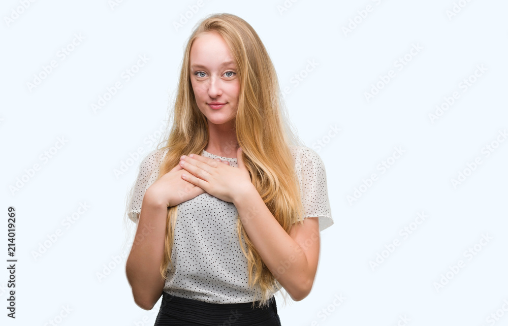 Blonde teenager woman wearing moles shirt smiling with hands on chest with closed eyes and grateful gesture on face. Health concept. Blonde teenager woman wearing moles shirt smiling with hands on chest with closed eyes and grateful gesture on face. Health concept.