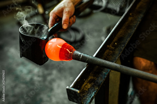 Glass-blower man working with hot orange glass to make a blown glass lantern