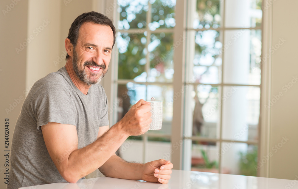 Middle age man drinking coffee in a cup with a happy face standing and smiling with a confident smile showing teeth Middle age man drinking coffee in a cup with a happy face standing and smiling with a confident smile showing teeth