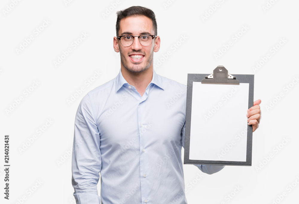 Handsome young business man showing a clipboard with a happy face standing and smiling with a confident smile showing teeth Handsome young business man showing a clipboard with a happy face standing and smiling with a confident smile showing teeth