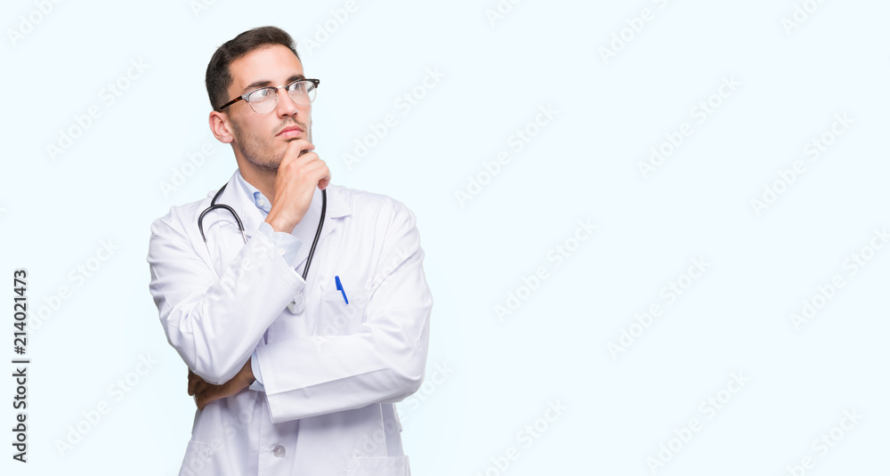 Handsome young doctor man looking confident at the camera with smile with crossed arms and hand raised on chin. Thinking positive. Handsome young doctor man looking confident at the camera with smile with crossed arms and hand raised on chin. Thinking positive.