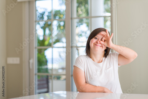 Down syndrome woman at home doing ok gesture with hand smiling  eye looking through fingers with happy face.