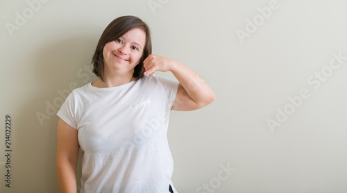 Down syndrome woman standing over wall smiling doing phone gesture with hand and fingers like talking on the telephone. Communicating concepts.
