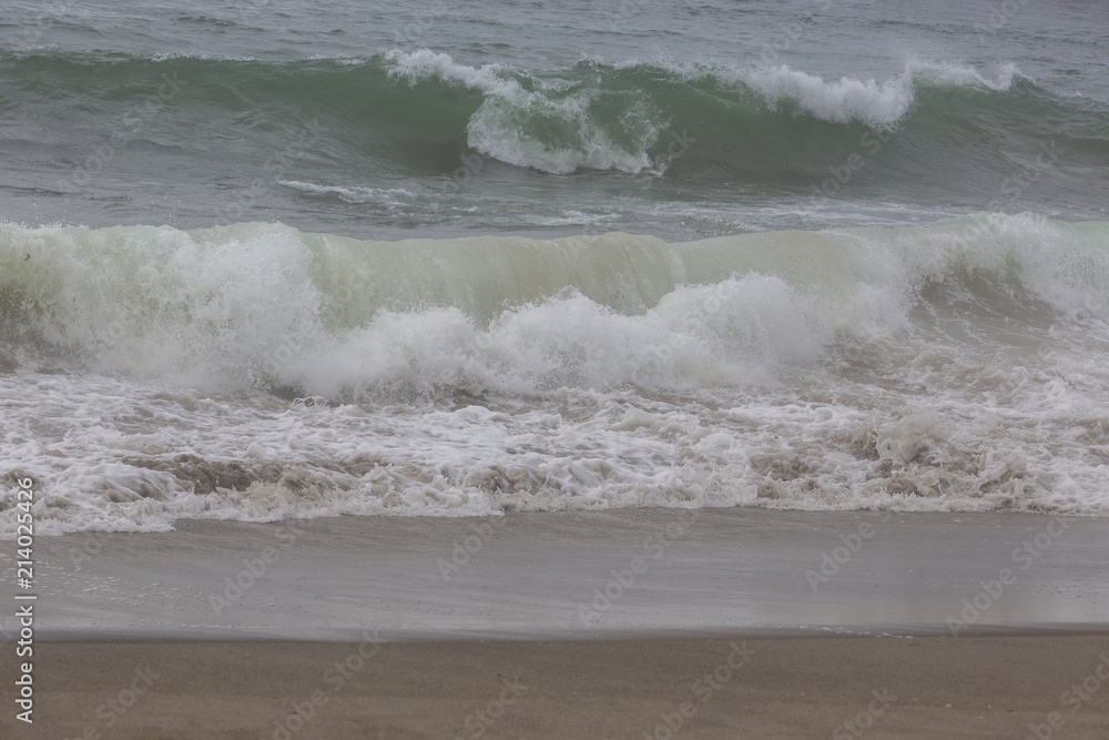 Incentive ocean wave on sandy beach. Overcast.