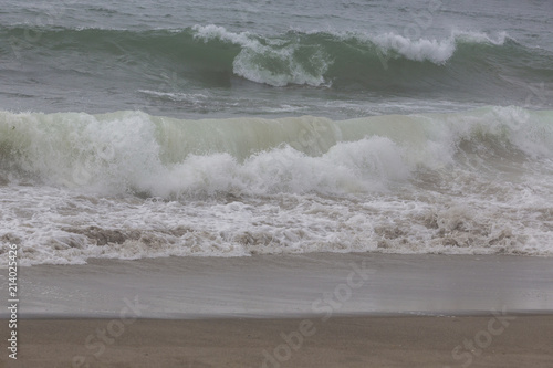 Incentive ocean wave on sandy beach. Overcast.