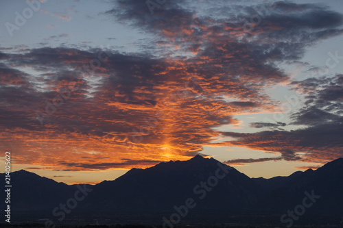 Early sunrise behind mountains. Orange colored clouds and dark silhouette of mountains.