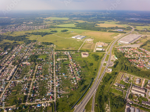 Helicopter drone shot. View from above on a small village, motor road, green forest and a large field on a warm, sunny summer day