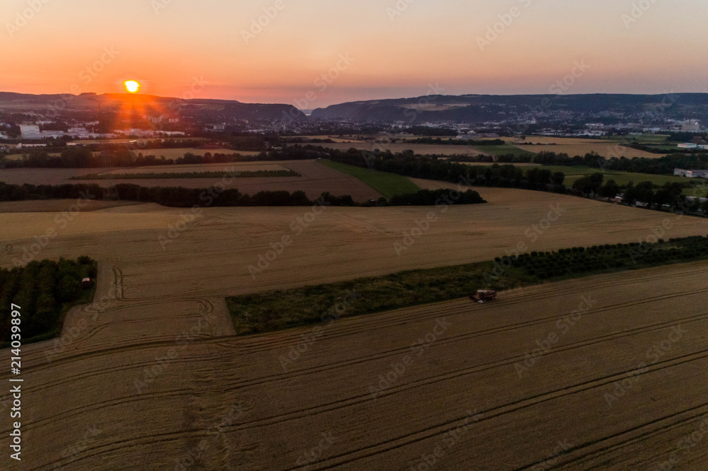 Fototapeta premium Aerial view of combine harvester harvesting an oats crop at sunset