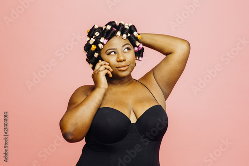 Woman with hair curlers and neglige talking on the phone and looking up, isolated on pink background