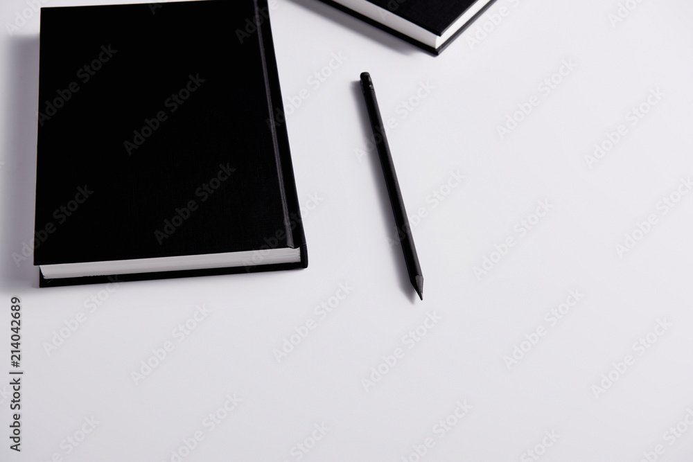 close-up shot of black hard cover notebooks with pencil on white surface close-up shot of black hard cover notebooks with pencil on white surface