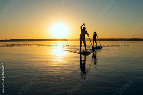 Silhouettes of men, friends paddling on a SUP boards