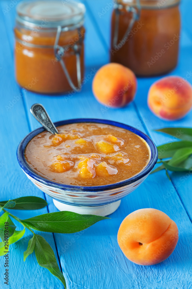 Bowl of apricot jam with spoon and fruit on blue table Bowl of apricot jam with spoon and fruit on blue table