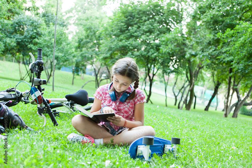 Fototapeta premium Girl reading a good book in the park next to her bicycle 