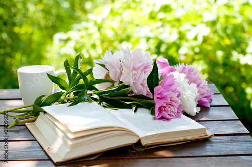 Book and cup of tea on a wooden table with flowers, summer garden, concept of relaxation and reading