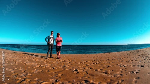 Two girls operating flying drone by wireless controller, beautiful sand beach, calm waves splashing