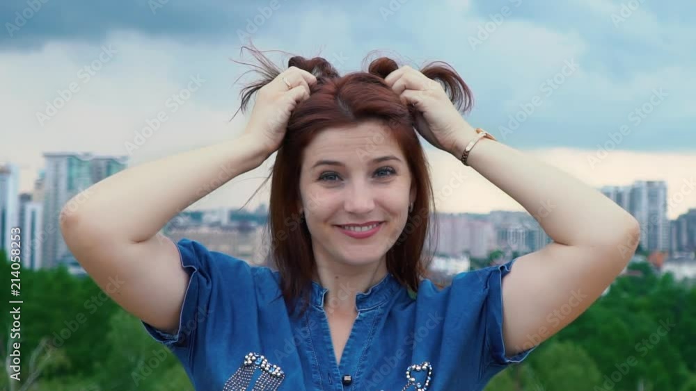 The girl fools around with her hair. Young woman playing her short red hair against the sky. Portrait of a girl The girl fools around with her hair. Young woman playing her short red hair against the sky. Portrait of a girl
