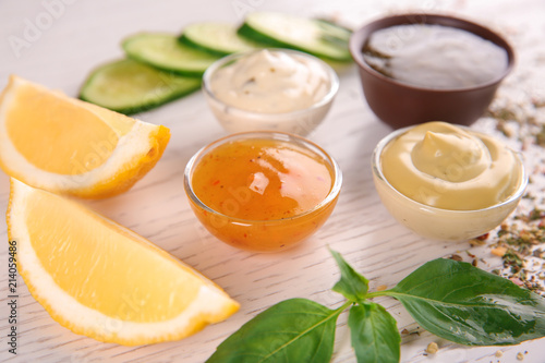 Bowls with different sauces and ingredients on light background
