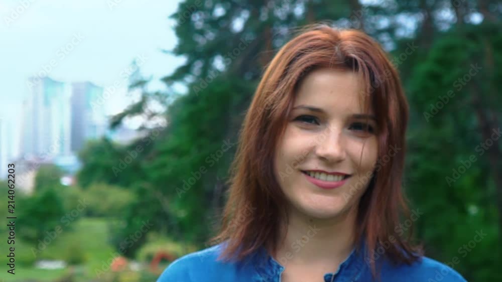 Portrait of a red-haired girl looking at the camera, against a background of green park trees, close-up Portrait of a red-haired girl looking at the camera, against a background of green park trees, close-up
