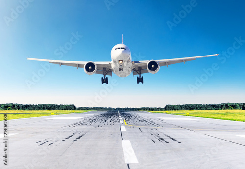 Passenger airplane with bright landing lights landing at in good clear weather with a blue sky on a runway.