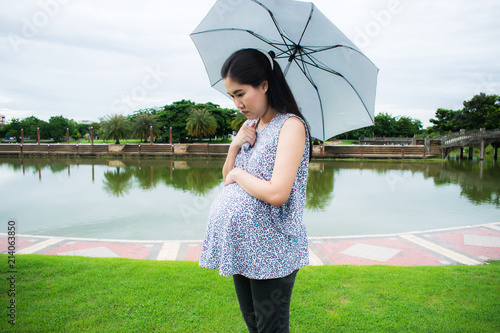 Принти на полотні Pregnant woman holding an umbrella at the park in the drizzly day