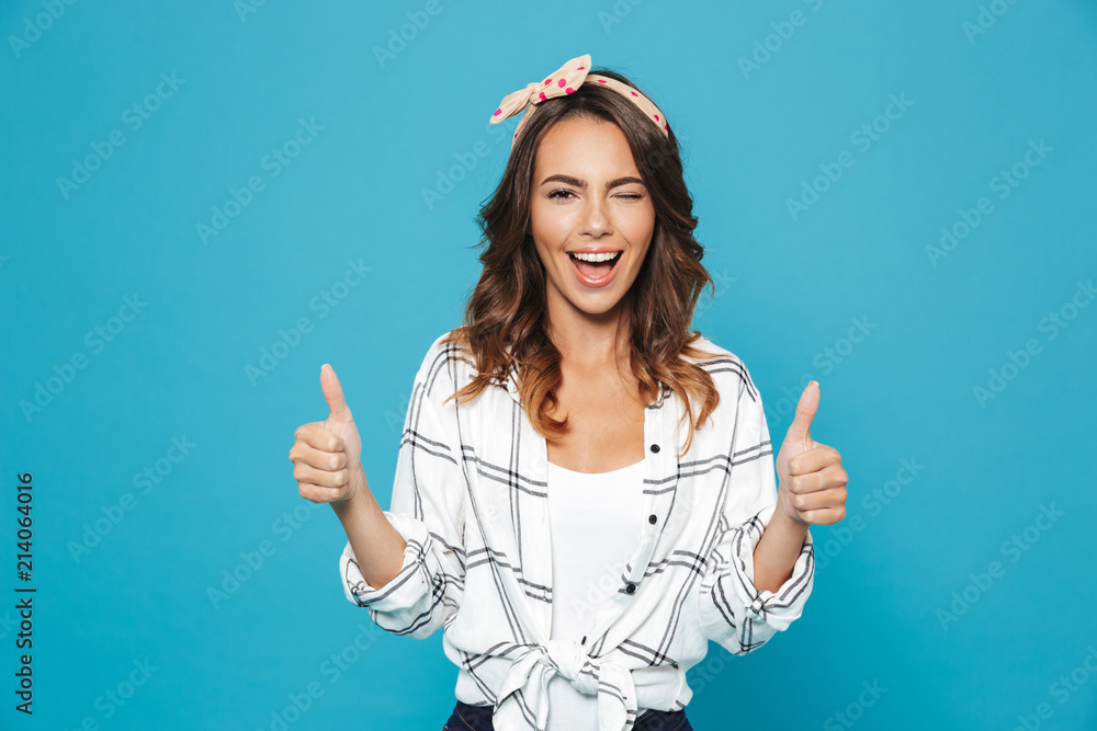 Portrait of lovely brunette woman 20s wearing headband smiling and showing thumbs up, isolated over blue background - obrazy, fototapety, plakaty 