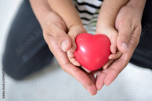 Child and adult person holding red heart, closeup. Adoption concept