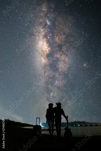 Couple traveler standing near the lake and looking milky way and stars on the sky at night.silhouette style.