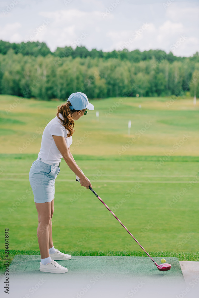 Fototapeta premium side view of woman in polo and cap playing golf at golf course