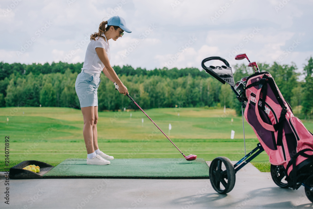 Obraz premium side view of woman in polo and cap playing golf at golf course