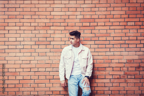 Stylish sexy man posing near brick wall in jeans looking away