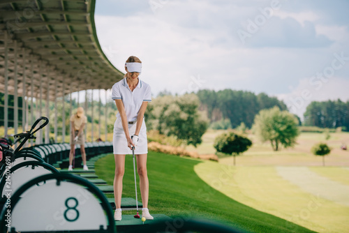 selective focus of smiling female golfer in polo and cap with golf club at golf course